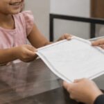 Um tutor e uma criança recebem uma certidão no balcão de um cartório, em um ambiente interno bem iluminado, com expressão de satisfação e clima institucional acolhedor.