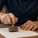 funcionário de cartório carimbando certidão em sua mesa, ambiente institucional com luz natural e plano médio