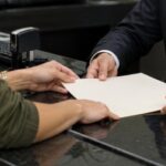 Pessoa entregando um documento a um atendente de cartório para realizar o registro, em um ambiente profissional e organizado
