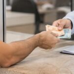 Uma pessoa entrega cédulas de reais a um funcionário de cartório durante um atendimento no balcão, em um ambiente institucional e organizado