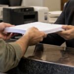 Pessoa entregando uma pilha de documentos a uma funcionária do cartório durante atendimento presencial