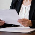 Funcionária de cartório analisando atentamente um documento em ambiente profissional, com iluminação natural e elementos de escritório ao redor